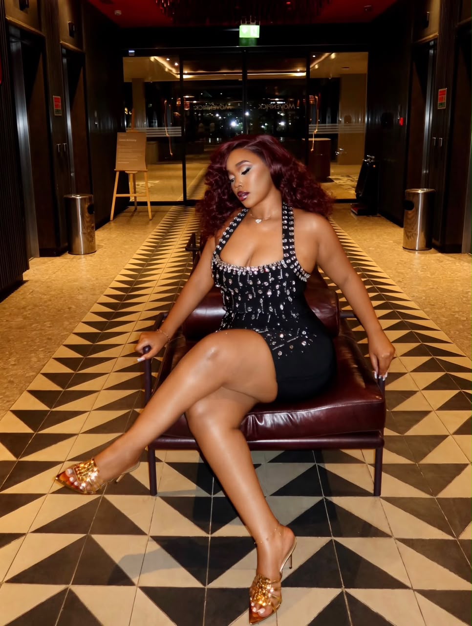 Nessahair customer wearing burgundy curls while seated in a black embellished dress