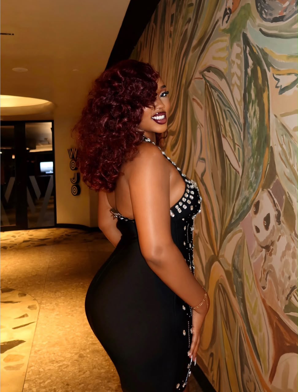 Side view of a Nessahair customer showing burgundy curls in a black embellished dress